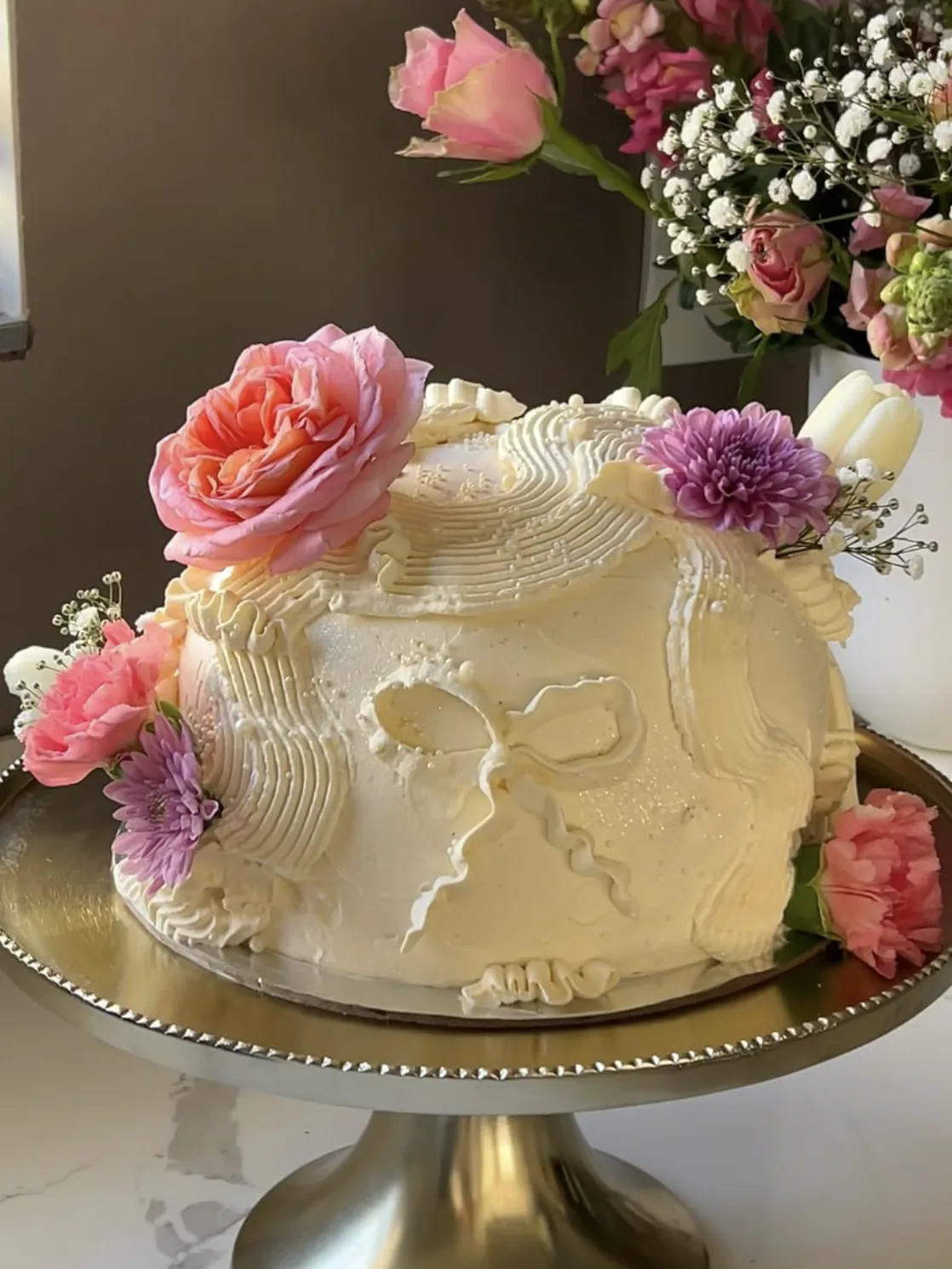A white buttercream cake topped with fresh roses, chrysanthemums and baby's breath