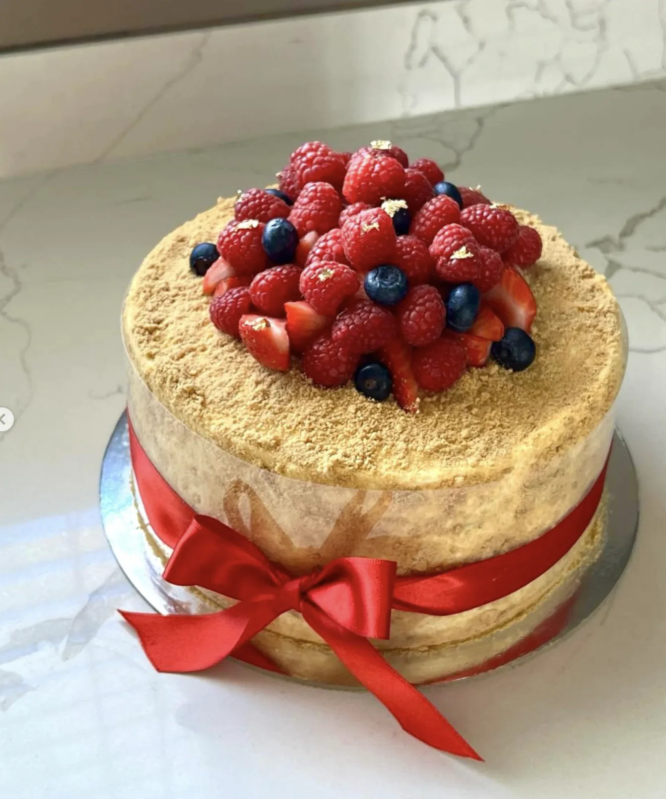 A honey layer cake topped with fresh raspberries, blueberries and edible gold leaf